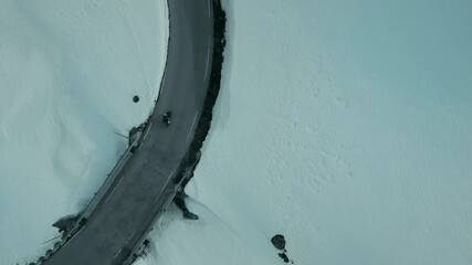 Drone shot of professional road cyclist on carbon bike ride on winter snow covered mountain road. Amateur hobby cyclist during hard effort training ride