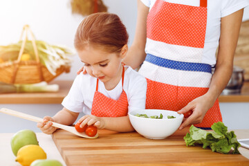 Happy woman and her daughter making healthy vegan salad and snacks for family feasting in sunny kitchen. Christmas, New year, Thanksgiving, Anniversary, Mothers Day. Healthy meal cooking concept