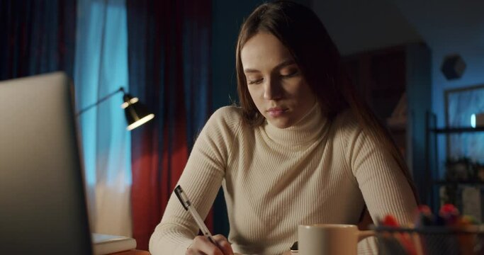 Young student speaking with friend using laptop, video conference call. Remote learning at night during coronavirus lockdown, sleepy woman doing homework, home isolation, freelancer home office.