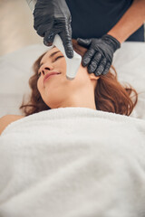 Beautician in black gloves reducing wrinkles on chin of client