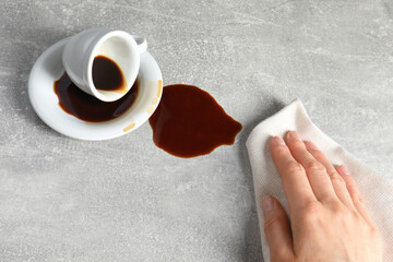 Woman wiping spilled coffee on grey table, closeup