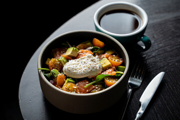 Gourmet salmon salad with avocado and a poached egg in a dark restaurant, top view