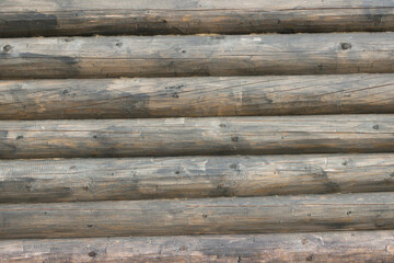 The wall of an old wooden house made of darkened weathered logs. Traditional Russian log hut.