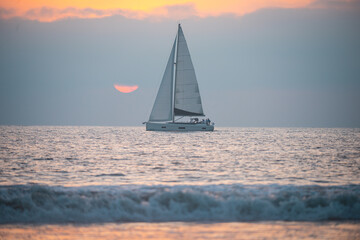 Naklejka na ściany i meble Yacht sailing against sunset. Landscape with skyline sailboat and sunset silhouette. Yachting tourism. Romantic trip on luxury yacht during the sea sunset. Ocean seascape.