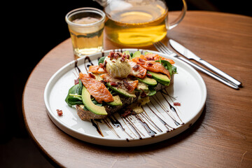 Healthy dietical snack in a cafe: salmon and avocado toast with a fresh poached egg, served with a pot of green tea