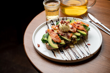 Healthy dietical snack in a cafe: salmon and avocado toast with a fresh poached egg, served with a pot of green tea