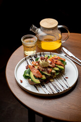 Healthy dietical snack in a cafe: salmon and avocado toast with a fresh poached egg, served with a pot of green tea