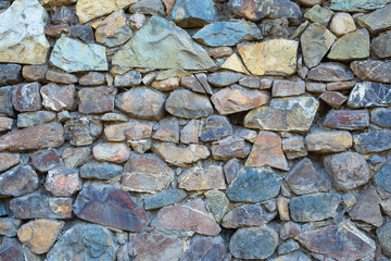 Frontal view of a wall composed of multi-colored brown, gray, brown, black, untreated stones, fastened with cement. .Stones of different shapes. .Texture, background. .