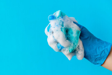 White foam on blue sponge clenched in hand above blue background with copy space.