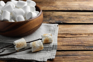 Sticks with roasted marshmallows on wooden table. Space for text
