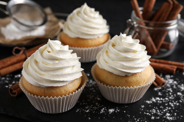 Delicious cupcakes with cream and cinnamon on black table, closeup