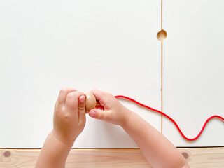 A child puts beads on a red rope. The development of fine motor skills, preschool education, the Montessori method. Lesson with the kid. Smart child. View from above. Nursery and kindergarten concept.