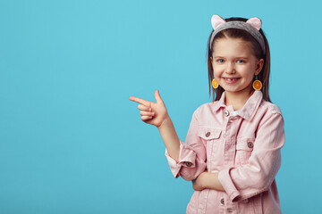 Cheerful girl smiling while pointing at blank space on blue background