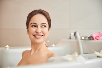 Obraz na płótnie Canvas Attractive brunette female enjoying taking bath with flowers