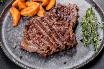 Delicious juicy fresh beef steak with spices and herbs on a dark concrete background