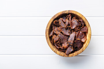 Sliced beef jerky. Dried beef meat in bowl on white table.