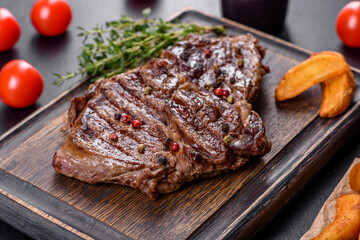 Delicious juicy fresh beef steak with spices and herbs on a dark concrete background