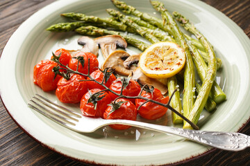 Baked asparagus with cherry tomatoes and lemon in a plate on a wooden background. Close-up.