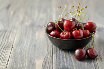 Fresh ripe garden cherry  berries in bowl closeup on a wooden aged table.