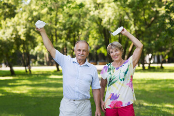 Obraz premium joyful elderly couple hold medical masks with hands up in the summer garden. end of a quarantine. vaccination. lockdown 