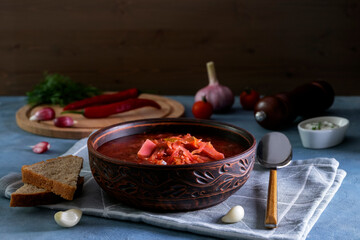 Close-up of the traditional Russian soup borscht made from cabbage, beets and other vegetables served in a clay ceramic plate with sour cream and garlic. National cuisine concept. Selective focus.