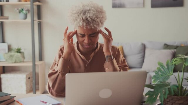 Serious thoughtful African American businesswoman at home office with laptop thinking of problem solution, feel headache temples massage tired female feeling discomfort after long working at computer