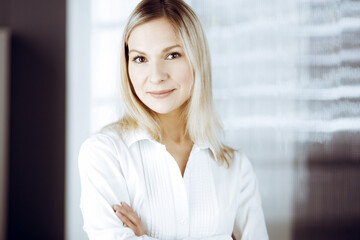 Friendly adult business woman standing straight. Business headshot or portrait in sunny office