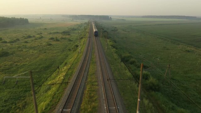 The train travels by rail through the open at dawn.