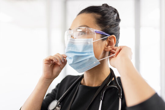 Female doctor in goggles putting on face mask
