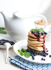 Breakfast with tea, pancakes, fresh blueberries and mint on white background. Fried pancakes on a white plate.