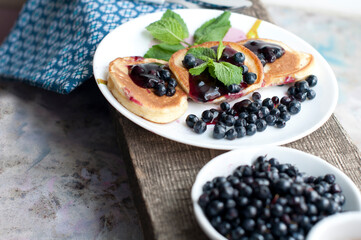 Breakfast with tea, pancakes, fresh blueberries and mint on wooden desk. Fried pancakes on a white plate