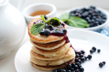 Breakfast with tea, pancakes, fresh blueberries and mint with jam on white background. Fried pancakes on a white plate with fork and knife.