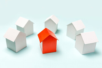 Fototapeta premium Simply design with miniature red toy model house in among white houses isolated on pastel blue background. Real estate property industry. Community unique neighborhood choice concept.