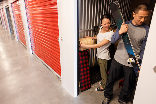 Couple moving skis and toboggan in storage facility locker