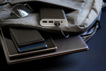 Portable charger - power bank lies in backpack along with sunglasses and gadgets - smartphones,...