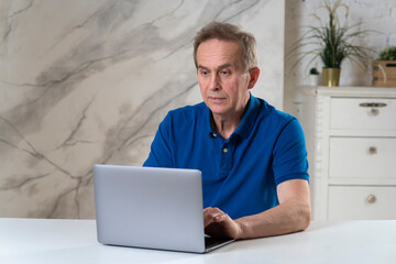 Portrait of surprised shocked amazed man, elderly senior male is working on laptop, having problem with using computer, looking at screen, typing. Retired people and technology concept.