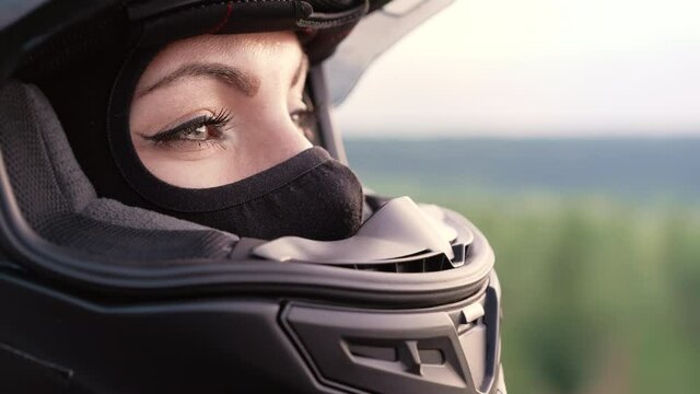 Portrait of confident motorcyclist woman in closed motorcycle helmet. Young driver biker looking away outdoors at sunset.