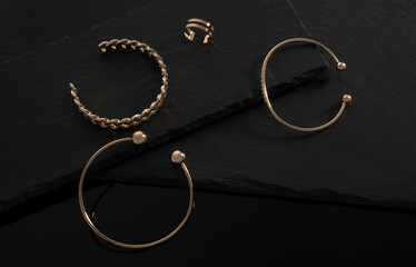 Fototapeta na wymiar three modern bracelets and double shape ring on black stone trays with copy space