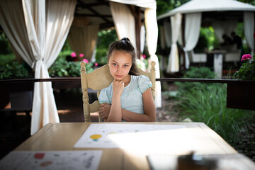 Preteen girl sitting in outdoors area of restaurant in summer