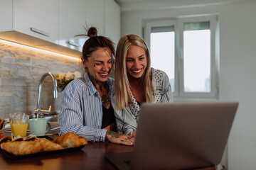 Lesbian couple in pajamas using laptop in the kitchen