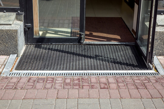 entrance to the store from a pedestrian sidewalk from a plink on a foot mat with storm drain grate, the facade of the exterior of a building close-up in sunny dry weather nobody.