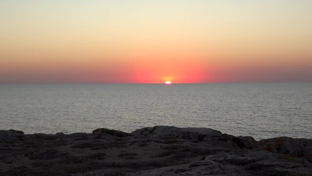 A magnificent sunset on the rocky seashore. The red sun was halfway down in the sea. Hitting the sun.