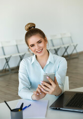 Young beautiful smiling businesswoman works in the office with a laptop and smartphone