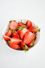 Red strawberries in a white glass bowl on a white background. Close up.