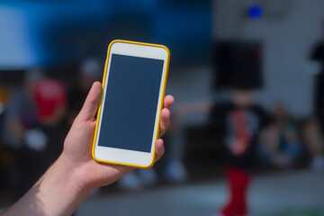 The guy holds a mock-up of a smartphone in his hand against the background of the children's dance...
