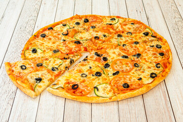 Large Vegan Pizza Sliced with Tomato Slices, Black Olives, Zucchini and Cheese Substitute on a Wooden Table