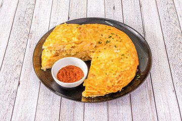 Spanish omelette with cheese and onion and red pepper sauce on circular black plate