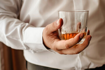 A man with a glass of whiskey in his hand wearing a white shirt. Relaxation after a hard day at...