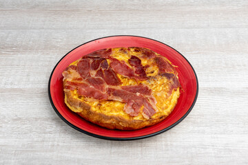 Spanish potato omelette with fried serrano ham inside a red plate