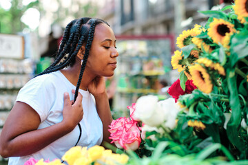 young latin woman smelling flowers at local market